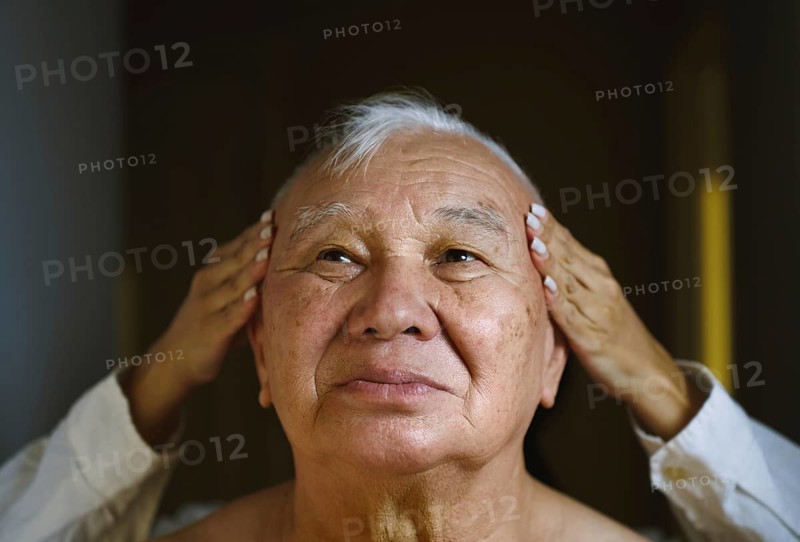 An elderly Asian man enjoys a soothing head massage His serene expression highlights a moment of relaxation and self-care, symbolizing well-being and tranquility