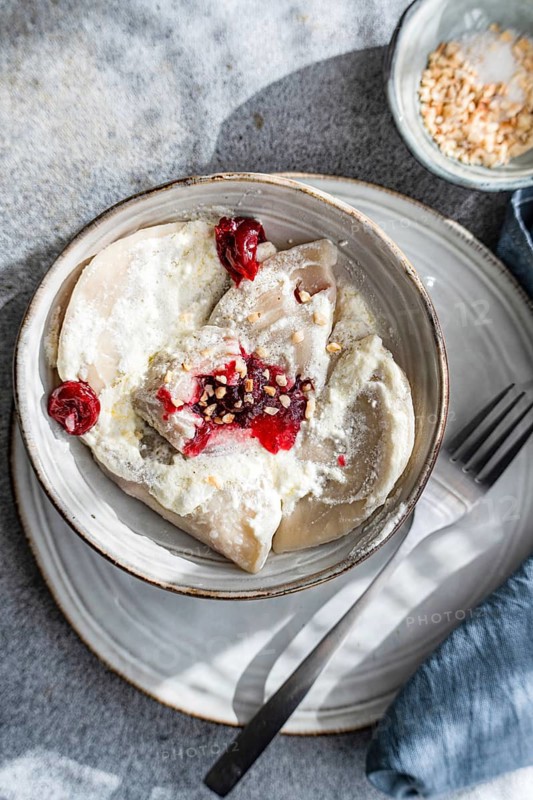 Traditional Ukrainian varenyky filled with cherries, served with creamy sour cream and sprinkled with chopped nuts. A delicious and authentic Eastern European treat