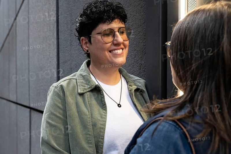 Curvy lesbian couple enjoying a heartfelt moment outdoors. They are standing close to each other, smiling warmly, conveying love and happiness in a city setting