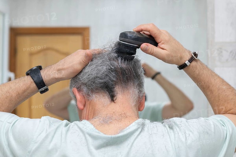 A man trims his hair with an electric trimmer while looking in a bathroom mirror. This scene captures the simplicity and convenience of a self-haircut routine at home