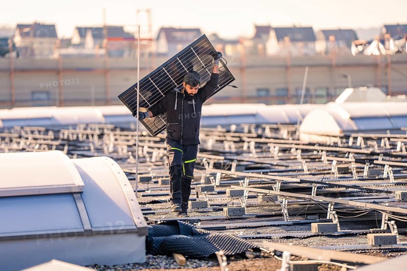 Worker with solar panel on a roof, clear conditions, protective clothing, PV installation at OBI Baumarkt, Mühlacker, Enzkreis, Germany