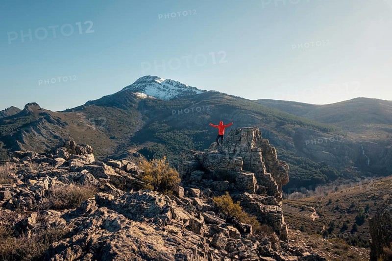 Back view of unrecognizable male hiker with arms wide open on a rock, celebrating his climb at the snow capped peak of Ocejon Mountain, Guadalajara, in the serene Sierra de Ayllon