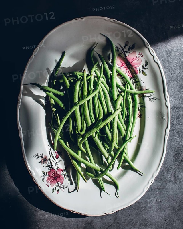 A cluster of green beans arranged elegantly on a vintage floral porcelain plate, capturing the essence of fresh vegetables. Natural light highlights their vibrant color