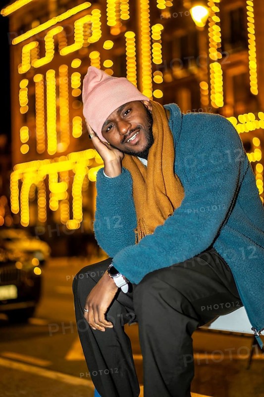 Vertical portrait of a cool african man posing sitting in the city in a Christmas night