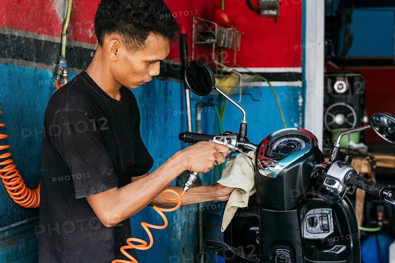 A skilled motorcycle cleaner uses specialized tools to meticulously clean and polish a motorcycle in a workshop setting. Perfect for illustrating vehicle maintenance concepts