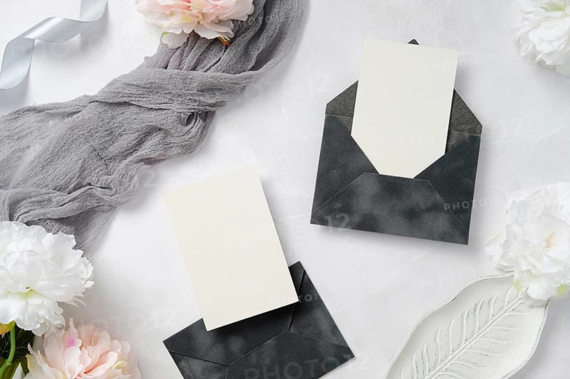 A sophisticated wedding stationery layout featuring elegant dark envelopes, blank cards, delicate flowers, and soft fabric, perfect for invitations or announcements