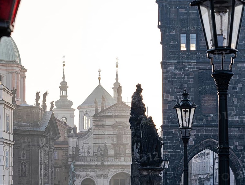 Early morning light bathes the historic statues and classic architecture of Prague in a warm glow, highlighting the blend of old European charm and heritage