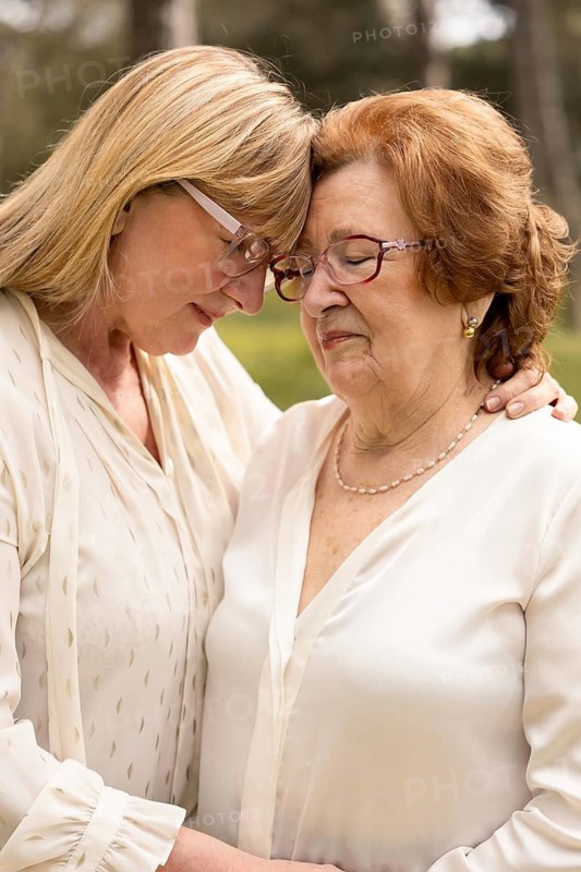 A touching moment between a mother and daughter as they share an embrace outdoors, highlighting their deep bond and connection. Both wear glasses, conveying love and warmth