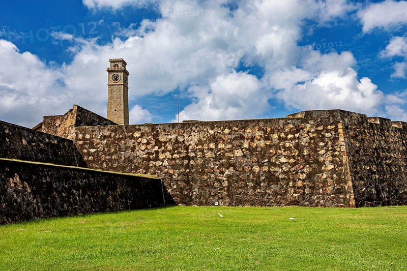 Tower and walls of an old fortress with green grass and cloudy sky, The fortress of Galle in Sri Lanka