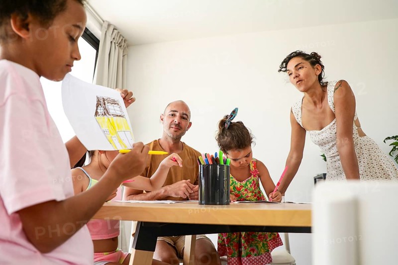 A family enjoys creative time together at home, engaging in a fun drawing session. Children and parents gather around a table, expressing themselves with art supplies