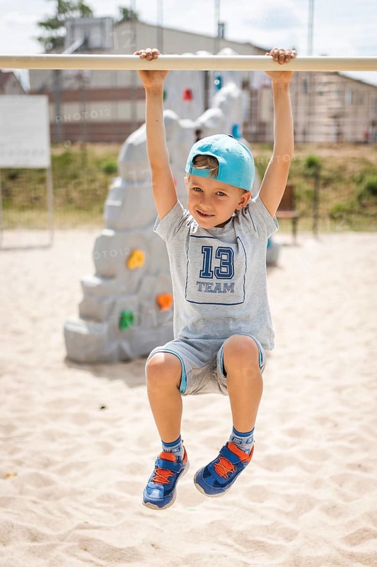 6-7 old boy hangs on the exercise bar in the playground