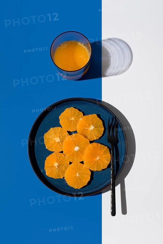 Fresh orange slices on a blue plate with a matching glass of orange juice. The vibrant contrast against a blue and white backdrop creates a sunny, refreshing vibe