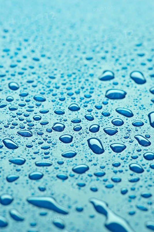 A detailed close up of water droplets on a smooth blue surface, showcasing the clarity and diverse sizes of the droplets. The image evokes freshness and tranquility