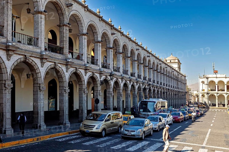 Buildings with arcades, cars and pedestrians on the street. Historic architecture in sunshine, The arcades at Plaza de Armas in Arequipa in Peru