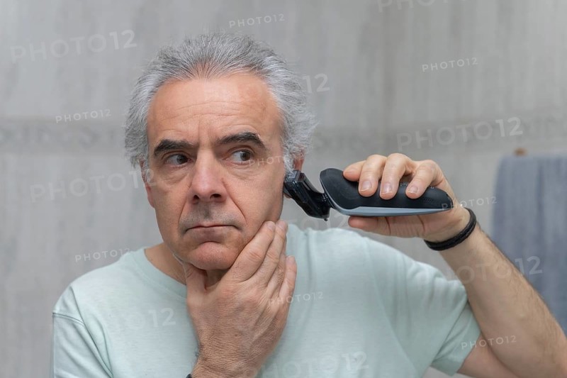 Mature man using an electric clipper for a home haircut. Focused on achieving a neat appearance and practicing self-grooming skills in a simple, DIY setting