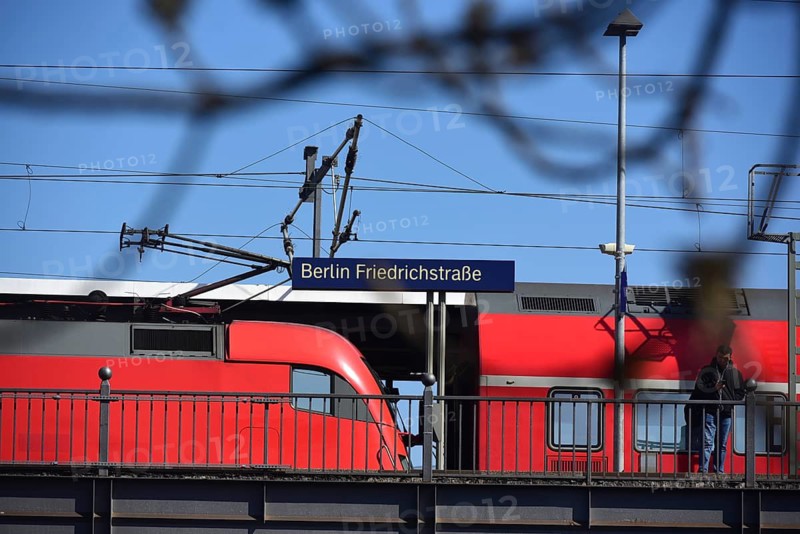 Berlin Friedrichstraße station train arriving at platform. A red train arrives at the platform of Berlin Friedrichstraße station, where commuters are waiting