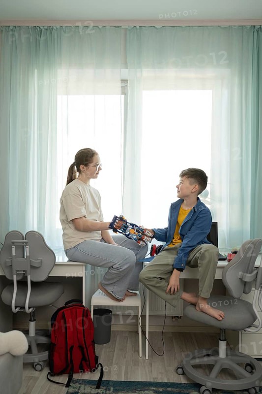 A boy and girl share a moment with a robotic hand. The setting is a cozy, bright room filled with educational materials that symbolize creativity and learning