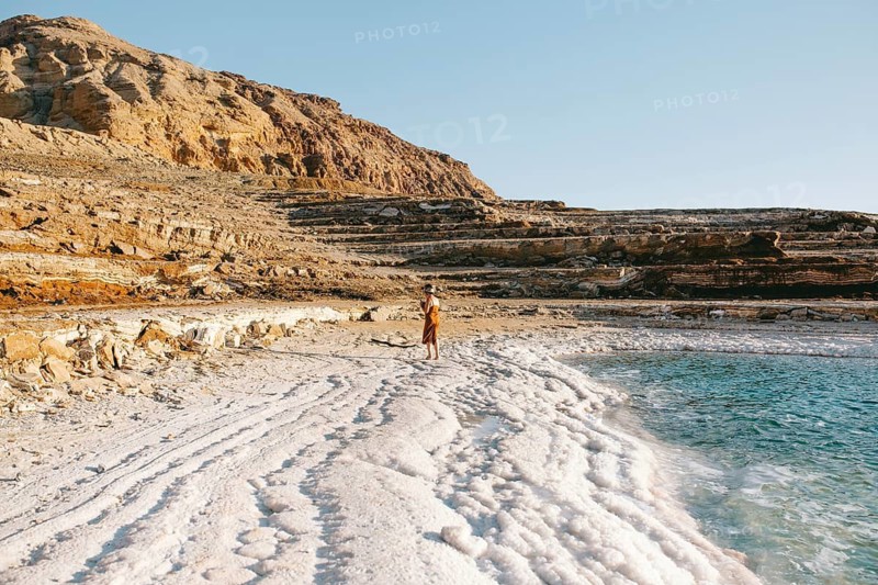 Back view of unrecognizable woman walking alongside the mineral-rich Dead Sea shores in Jordan during a serene sunset
