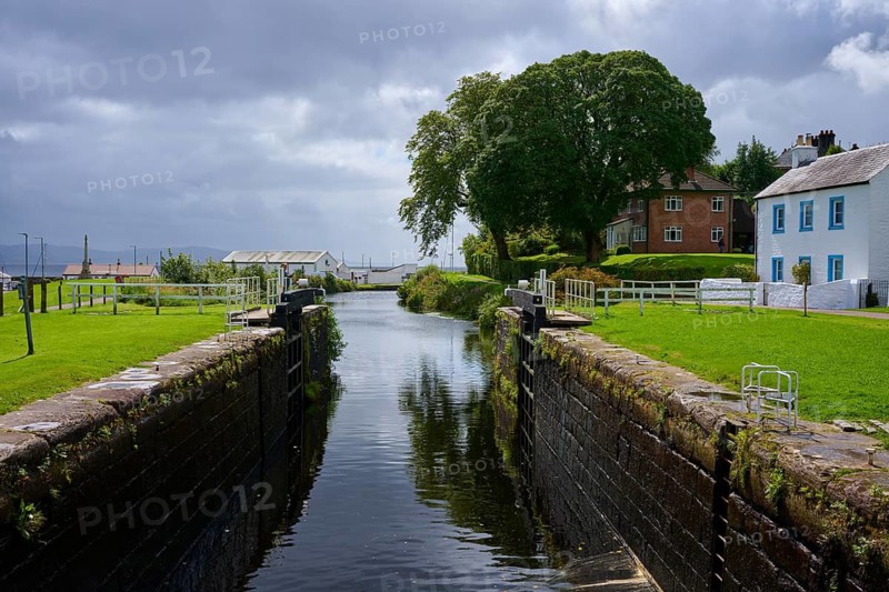 Canal with lock surrounded by lush trees and houses under a cloudy atmosphere, Ardrishaig, Caledonian Canal, Loch Fyne, Scotland, United Kingdom, United Kingdom