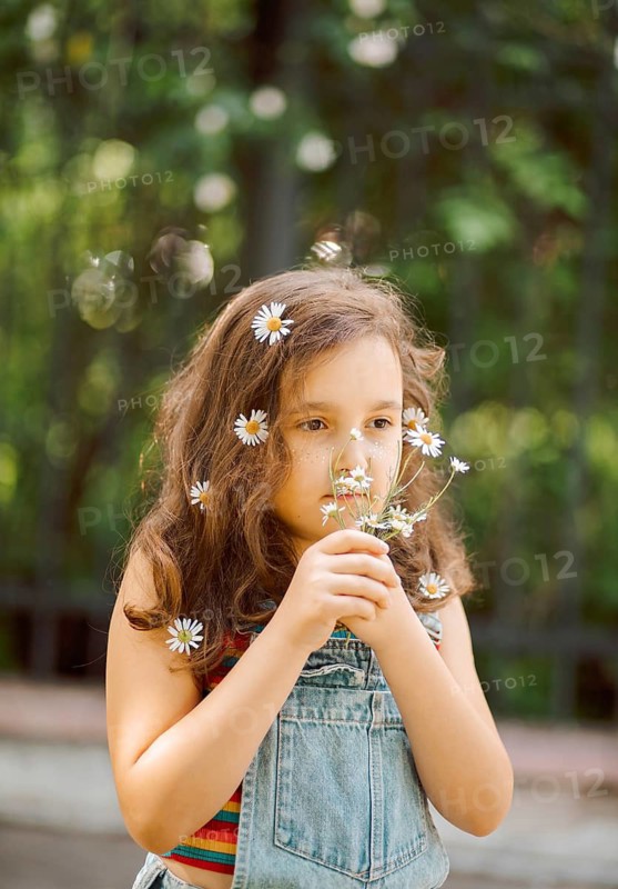A young girl holding chamomile flowers in a sunny meadow. Her expression reflects the beauty and innocence of childhood, surrounded by greenery and sunlight