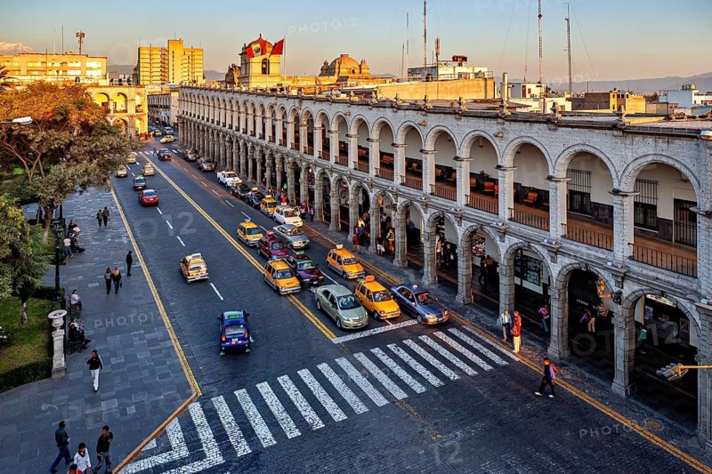 Urban scene at sunset, historic arcades, busy street with traffic and flags, The arcades at Plaza de Armas in Arequipa in Peru