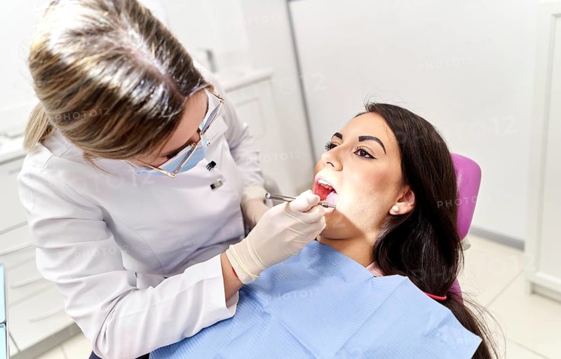 A dental professional examines a patient in a modern clinic, using specialized tools to ensure oral health. The setting is bright and clean, emphasizing a caring environment