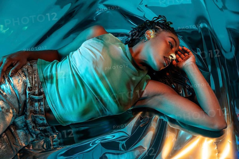 A futuristic African young woman reclines gracefully in a vibrant, abstract metaverse environment, showcasing a blend of technology and art. Her presence exudes creativity and innovation