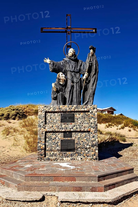 Statue of monks with cross in a sandy landscape under clear sky, monument by Francisco De Paola in Puerto Madryn in Argentina