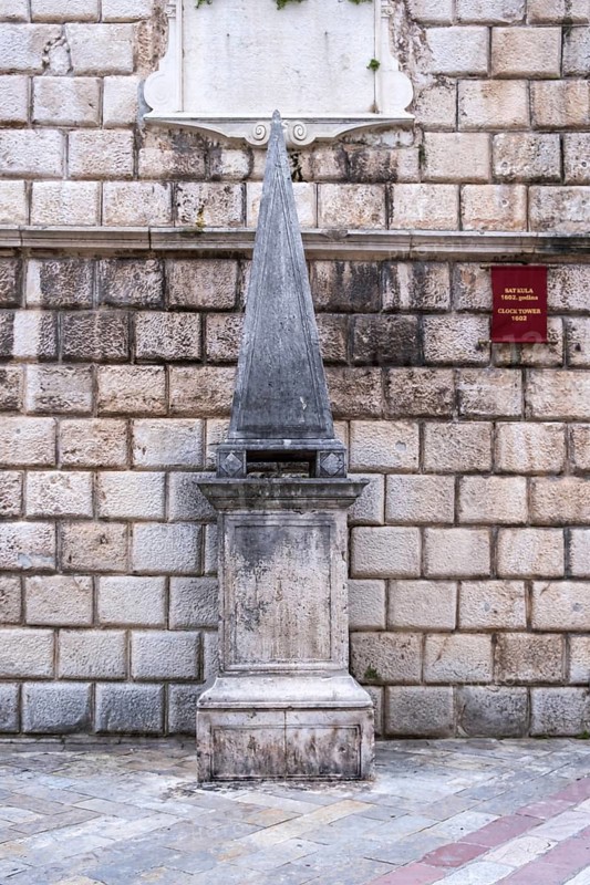 Medieval pillory stands in front of the 17th century clock tower, Old Town Kotor, Montenegro, Balkans
