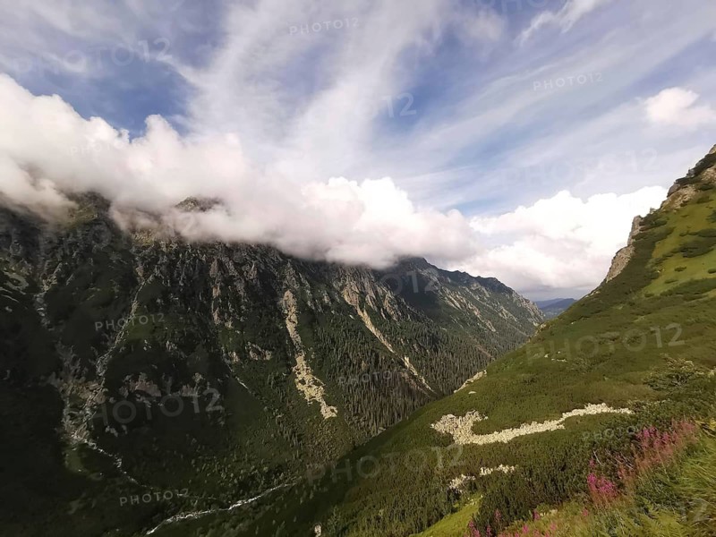 Extensive valley with lush slopes under blue skies with thick clouds above the mountain peaks, Zakopane, hiking in the High Tatras National Park, Carpathian Mountains, Poland