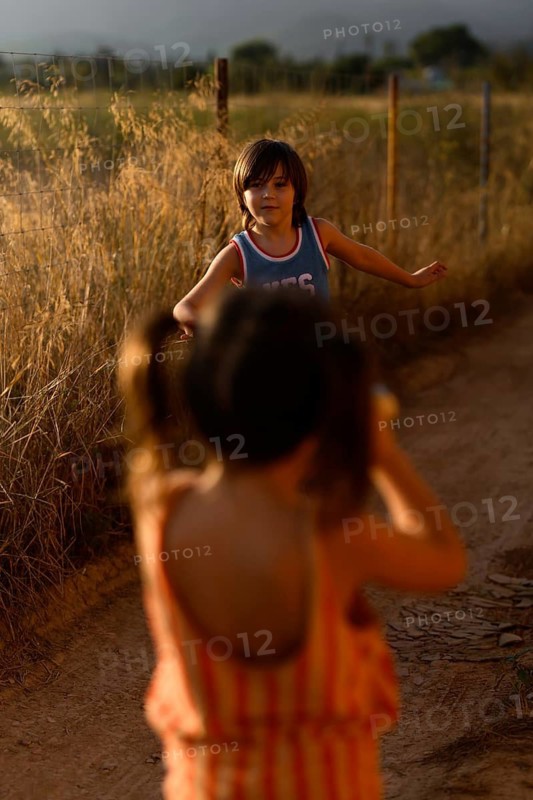 Two children joyfully play on a dirt path in Santa Maria del Cami, Mallorca, surrounded by golden fields under warm sunlight, capturing the essence of summer play