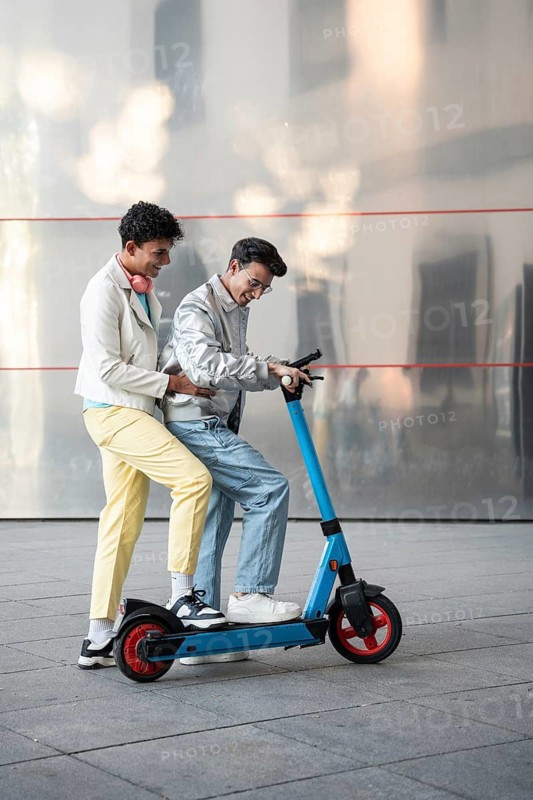 A happy gay couple shares a joyful moment riding an electric scooter on a sunny day. They smile, enjoying the ride, illustrating love and camaraderie
