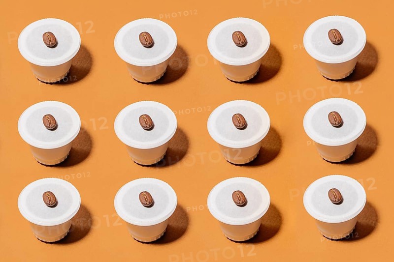 A neatly arranged grid of biodegradable coffee pods, each topped with a coffee bean, set against a vibrant orange background. The image highlights symmetry and contrast