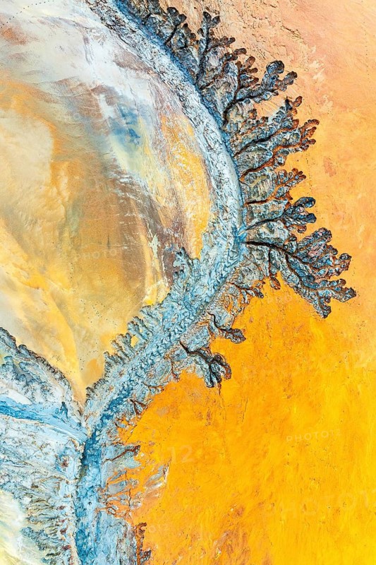 Aerial view showcasing intricate fractal patterns formed by mud and minerals. The vibrant earthy tones create a mesmerizing abstract landscape, evoking natural artistry