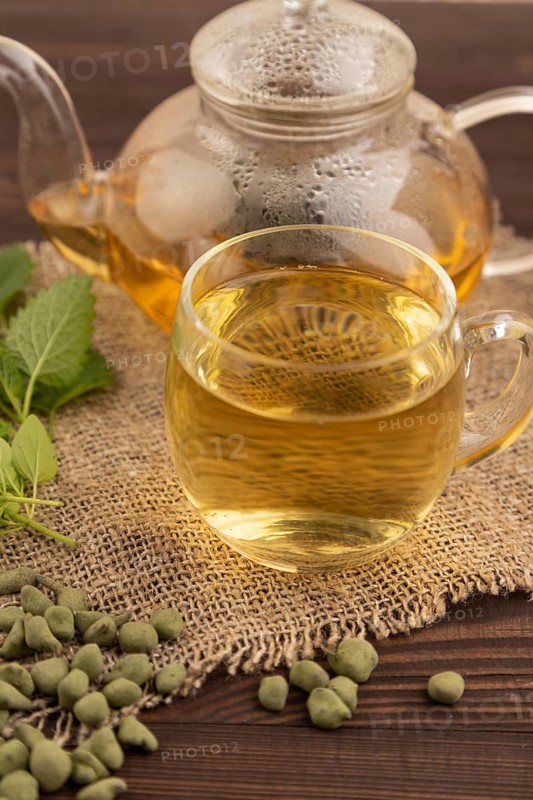 Green oolong tea with herbs in glass on brown wooden background and linen textile. Healthy drink concept. Side view, close up, selective focus