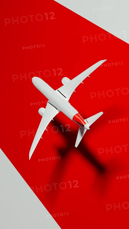 A sleek commercial airplane soars through the sky, casting a distinct shadow on a vibrant red background