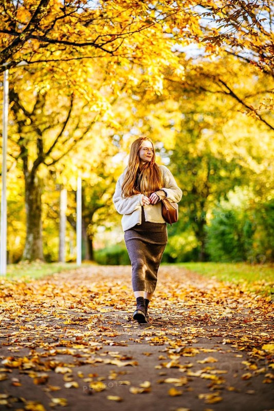 Beautiful pregnant woman with long red hair strolling peacefully through a picturesque autumn park, surrounded by golden leaves and soft sunlight, capturing a serene moment