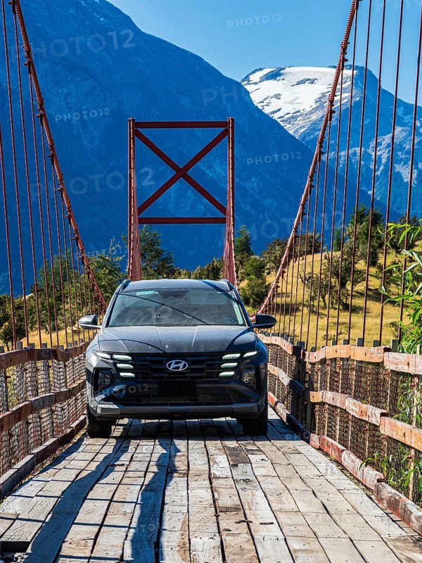 SUV driving over old-style orange suspension bridge, river Rio Nadis south of Cochrane, mountain range in the back, Patagonia, Chile