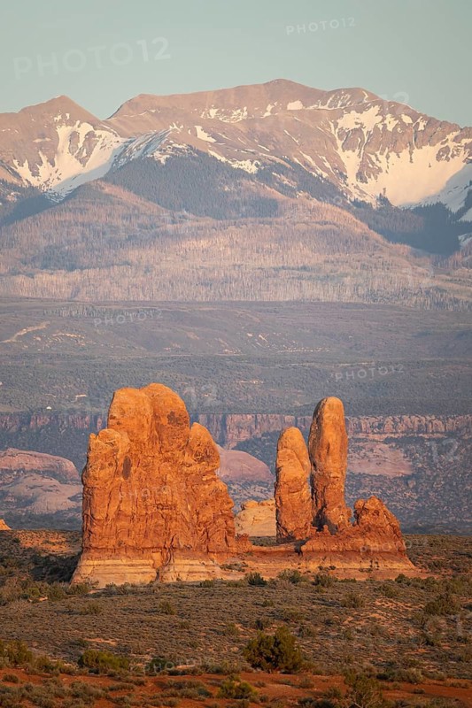Stunning landscape of Arches national park with unique rock formations set against a backdrop of snow-capped mountains, showcasing the park's rugged beauty at sunrise