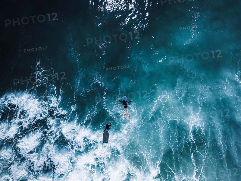 Aerial view of a surf session in Portugal, featuring surfers navigating the vibrant blue waves. The dynamic scene captures the thrill of surfing in the open sea