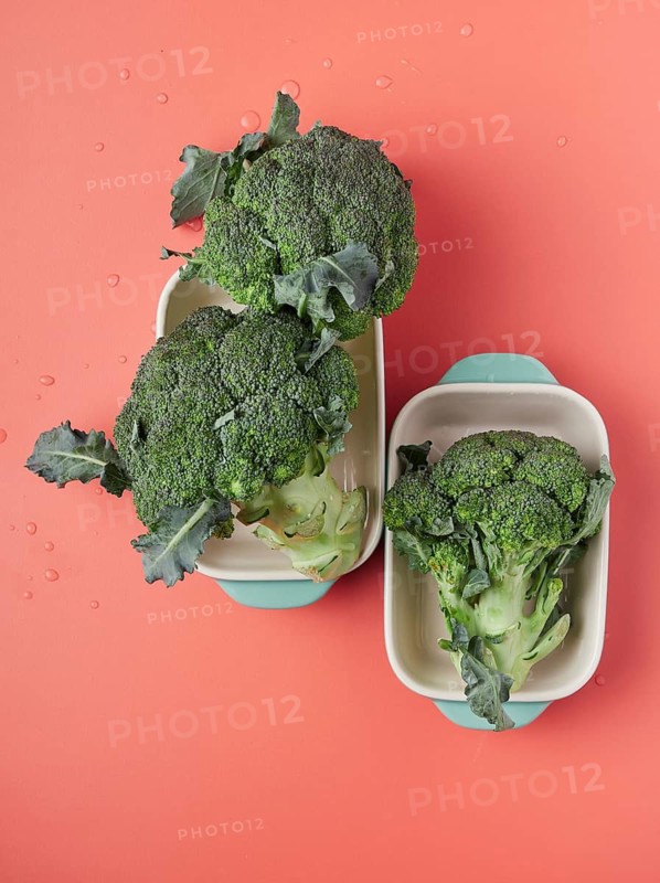Whole fresh broccoli pieces on baking pans on a pink table