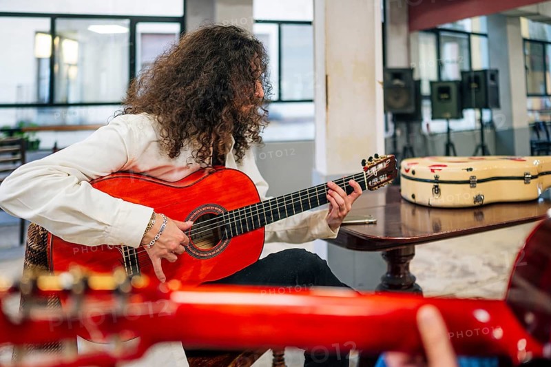 Latin man with long hair playing red bass guitar in studio