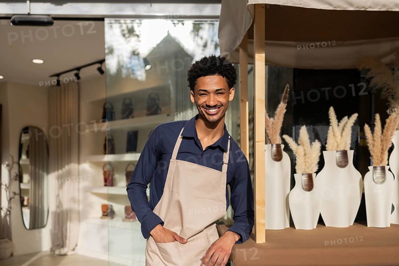 A cheerful store employee wearing an apron stands in a chic bag store, surrounded by stylish bags and modern decor, creating a friendly and inviting atmosphere for shoppers