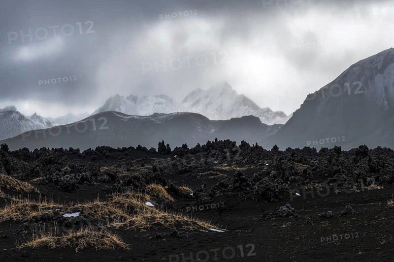 Moody skies loom over the rugged, volcanic terrain of Iceland's Highlands. Snow-dusted peaks rise in the distance, creating a dramatic and awe-inspiring landscape
