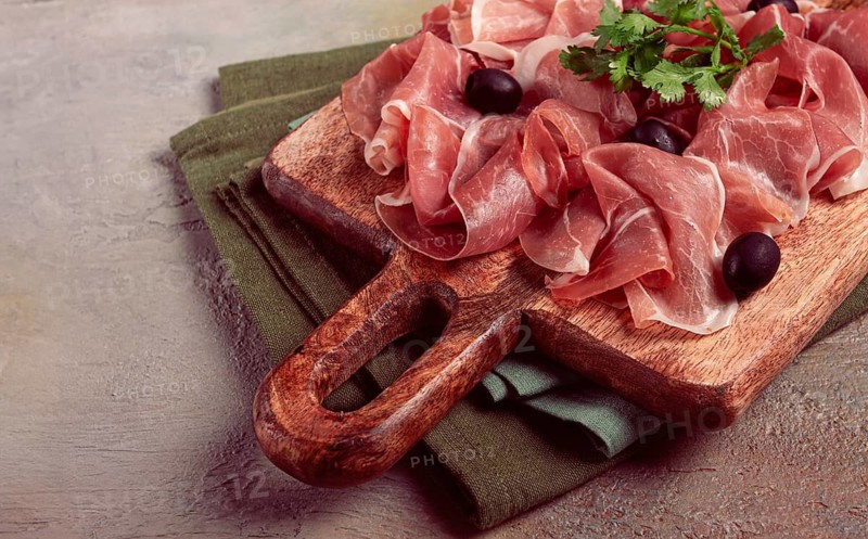 Sliced prosciutto, on a cutting board, with olives and herbs, snack, breakfast, no people