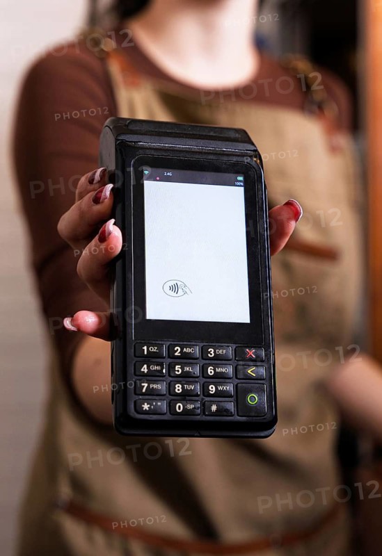 A woman offers a contactless payment terminal in a cozy cafe setting, highlighting modern convenience and efficient service. Perfect for themes of technology and hospitality