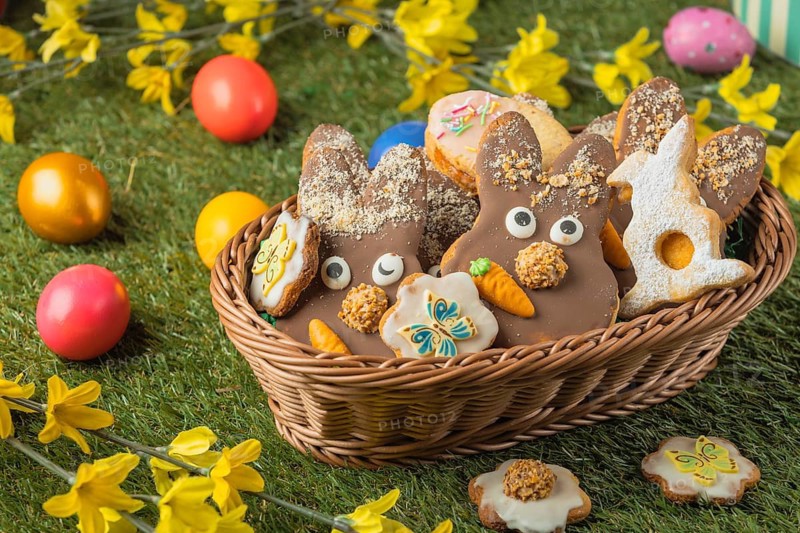 Decorated Easter cookies in a basket surrounded by colorful eggs on grass