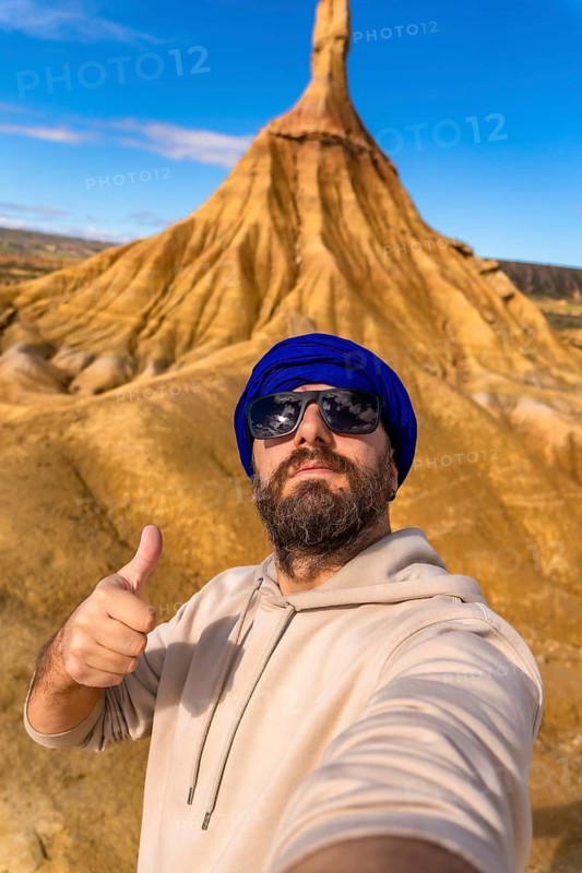 Tourist wearing sunglasses and a blue turban is taking a selfie while gesturing thumbs up in the bardenas reales desert, navarre, spain