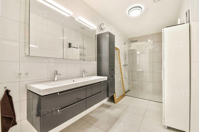 Spacious modern bathroom featuring a large walk-in glass shower, sleek double sink vanity with ample storage, white tiled walls, and minimalist lighting fixtures for a clean look