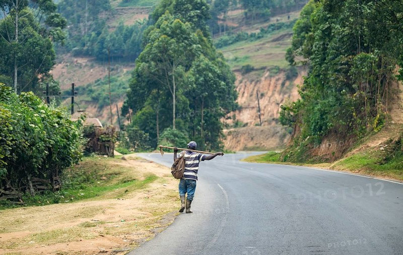 Man in rubber boots and with rake walking along a road, farmer in rural Uganda, western region, Uganda